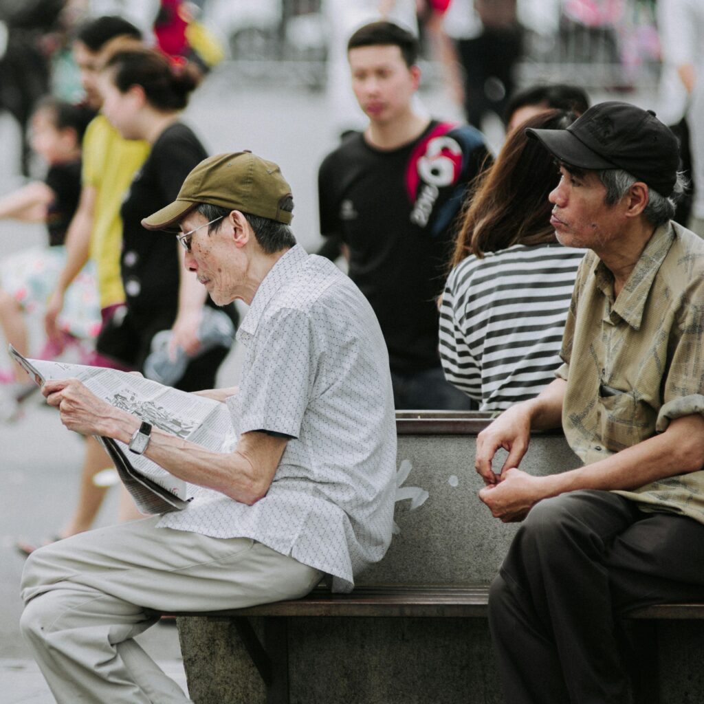 Two senior men sitting on a bench in a bustling city park, enjoying leisure time.