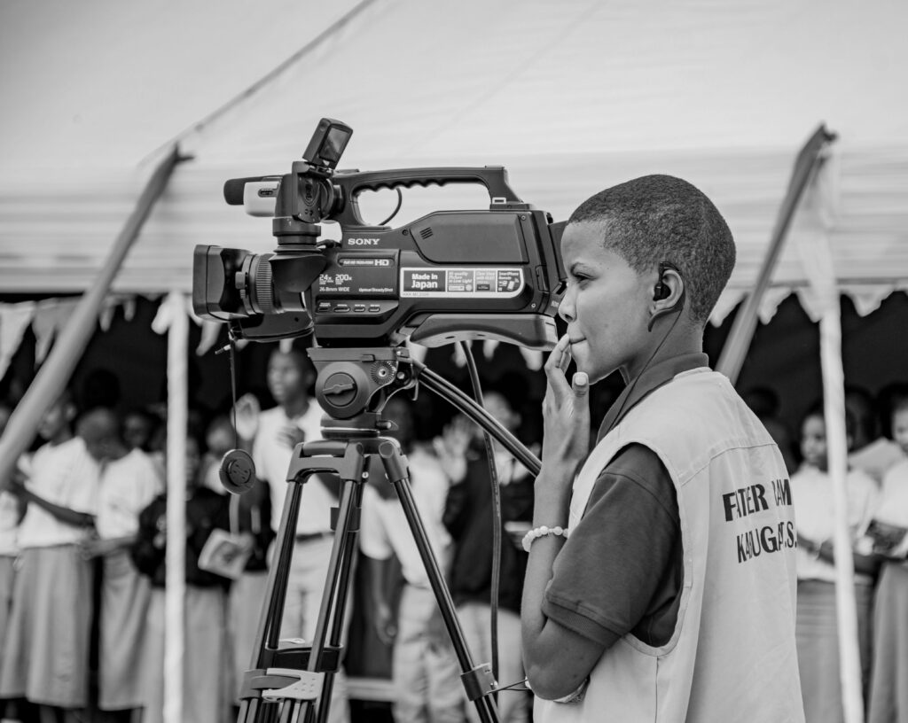 A young person operates a professional video camera at an indoor community event.